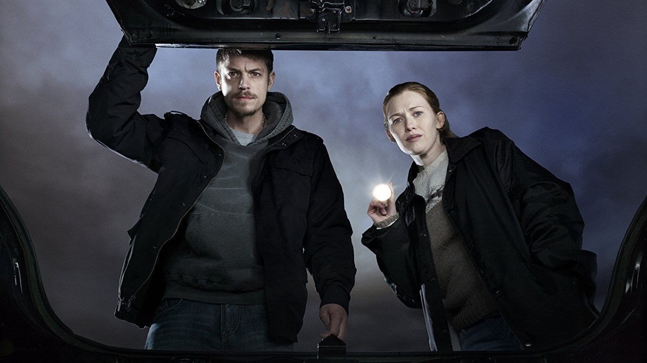 Mireille Enos and Joel Kinnaman in The Killing, looking into a car trunk with a torch