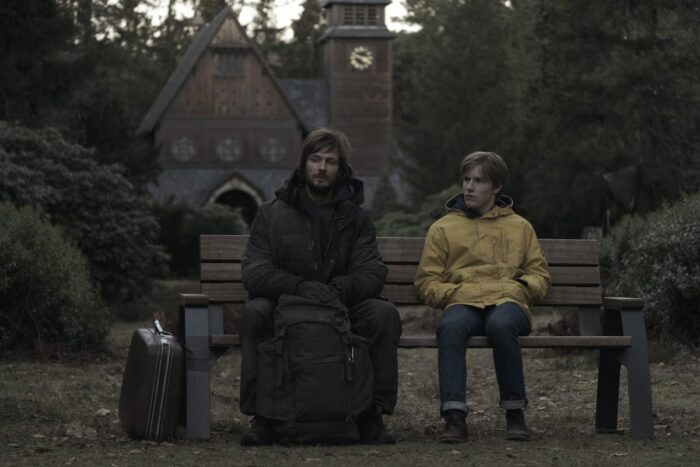 Young Jonas sits on a bench next to older Jonas in Dark on Netflix