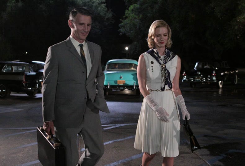 Betty and Henry walk through a car park together at night, smiling