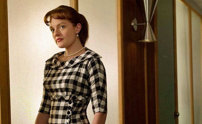 Peggy Olson standing in a door way wearing checkered print dress