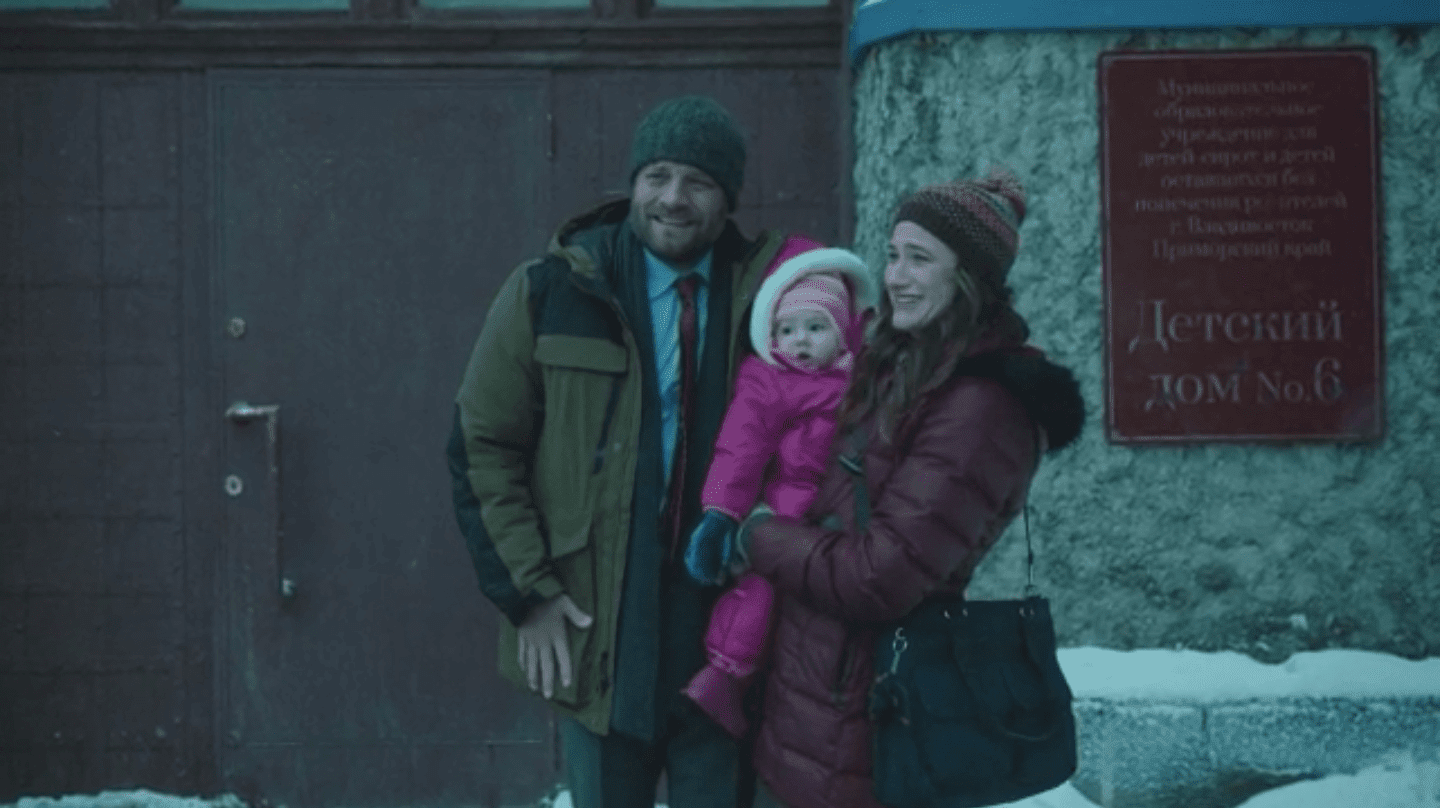 a man and a woman pose for a photo with their adopted baby in the cold outside a Russian orphanage joe anka kathryn hahn jay r. ferguson The Romanoffs
