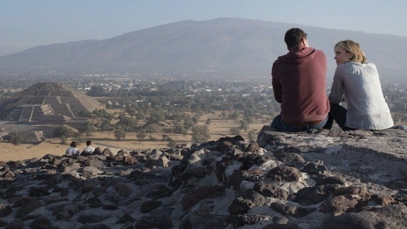 a man and a woman sit overlooking Mexican pyramids at Teotihuacan