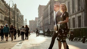 a man and a woman walk across a street in sunshine