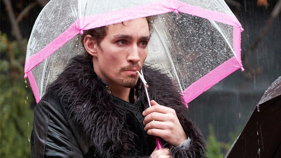 Robert Sheehan as Klaus Hargreeves standing in the rain under an umbrella