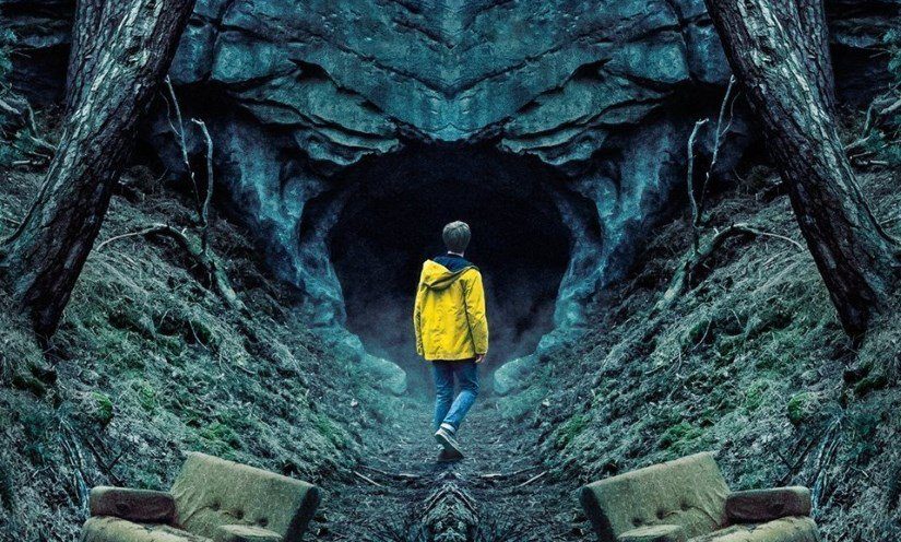 A teenage boy in a yellow coat standing next to chairs and looking into a cave