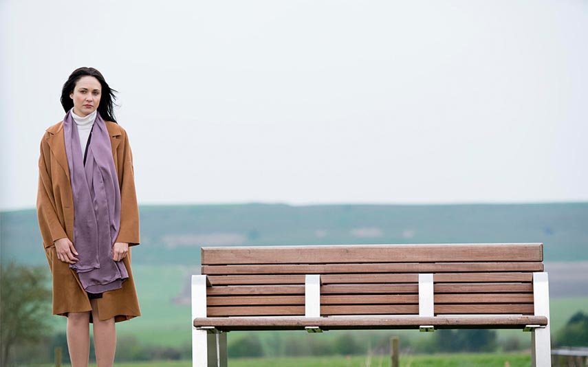 Lisa stands outside by a bench near a field