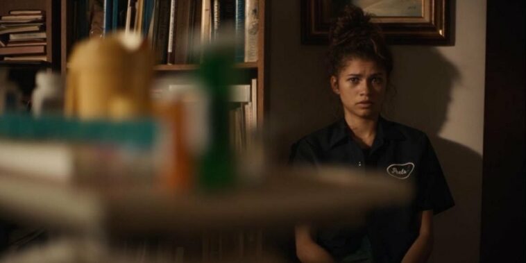 Rue (Zendaya) looks stricken at pill bottles that are blurred in foreground of image.