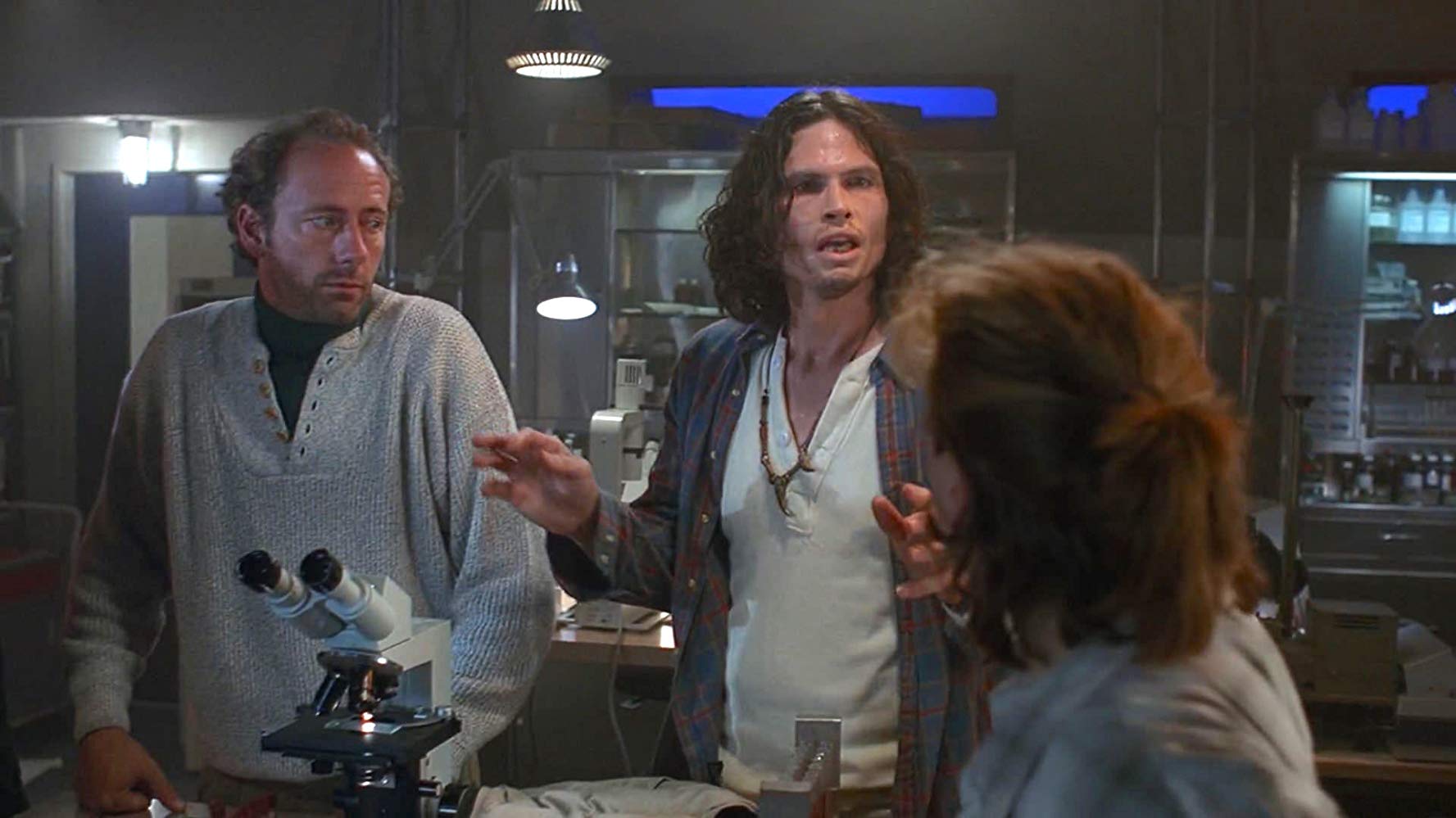 One hostile-looking man talking to two other people in a lab.