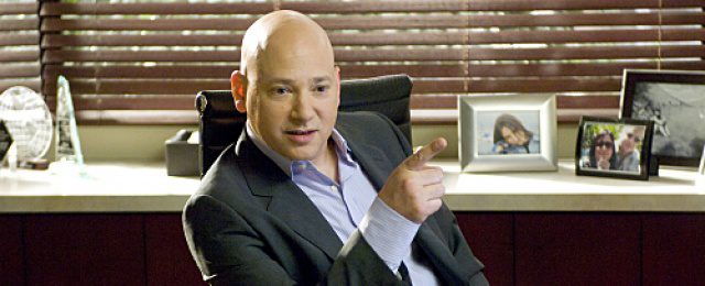 Evan Handler sits in a chair pointing his finger