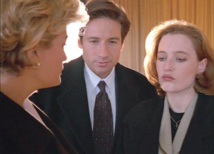 Detective White speaks to Agents Mulder and Scully, while Scully looks down disdainfully.