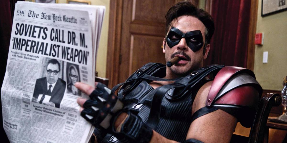 Image from Watchmen 2009 film with Comedian in armored costume and with cigar in mouth looking away from newspaper he is holding with headline "Soviets call Dr. M. Imperialist Weapon."