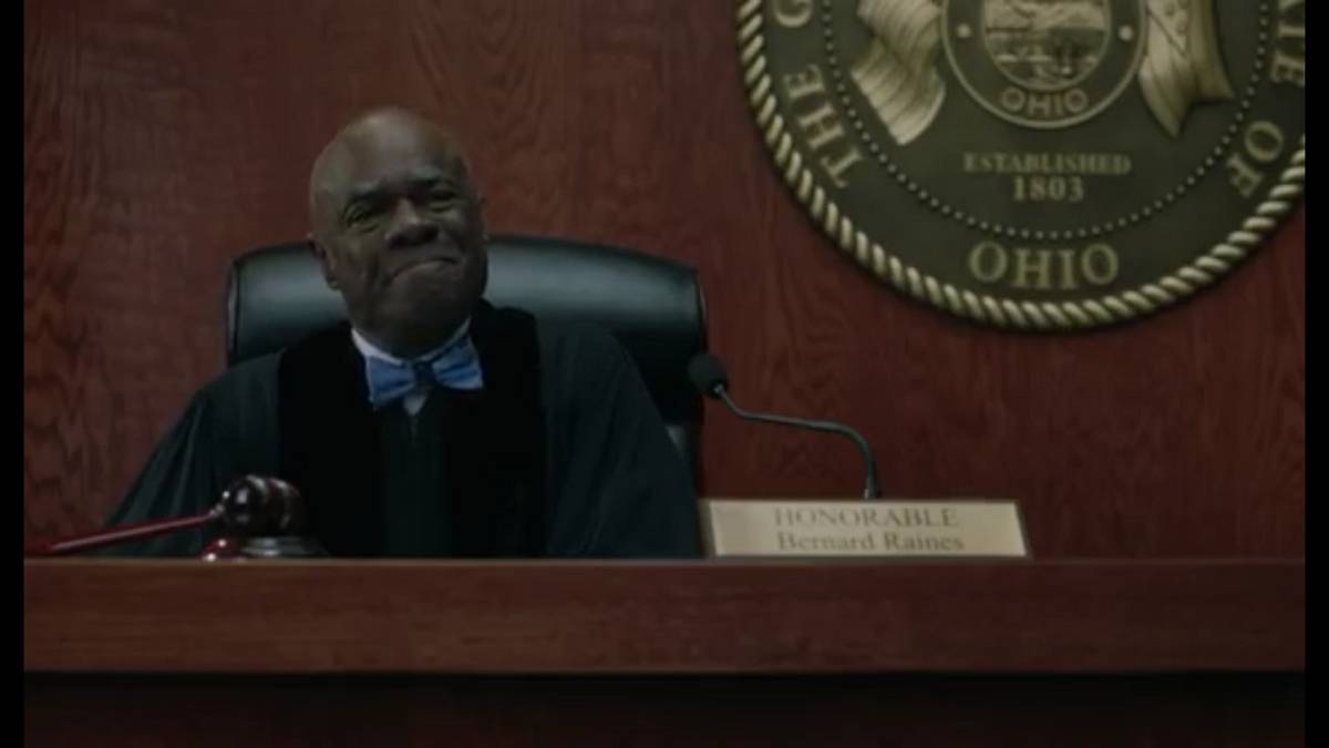 Judge Raines, in robes and a blue bowtie, sits behind the bench, with the Seal of the State of Ohio hanging on the wall behind him.