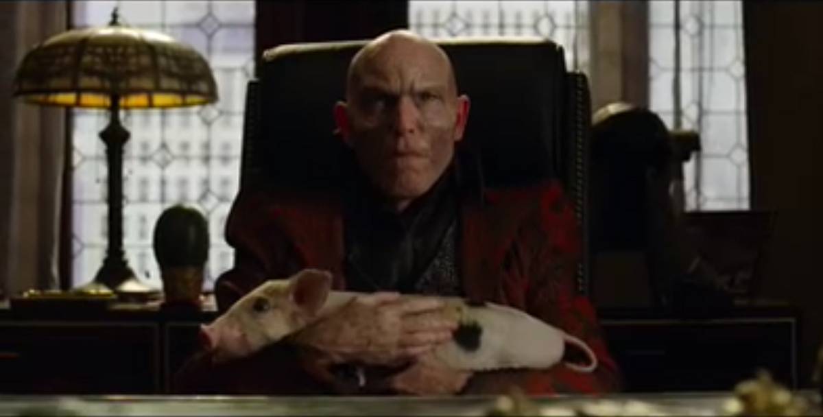The Terror sits in a high-back leather chair with a young piglet on his lap. 