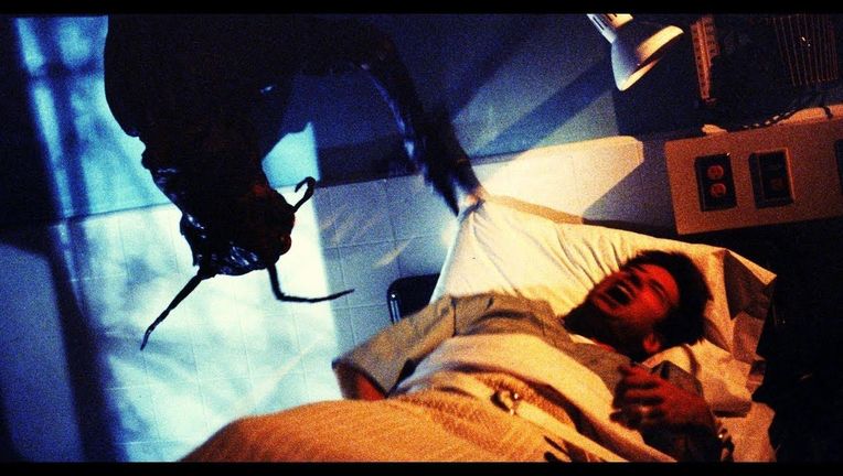 Agent Fox Mulder is screaming, restrained to a hospital bed, while the insect monster dangles above him from the ceiling.