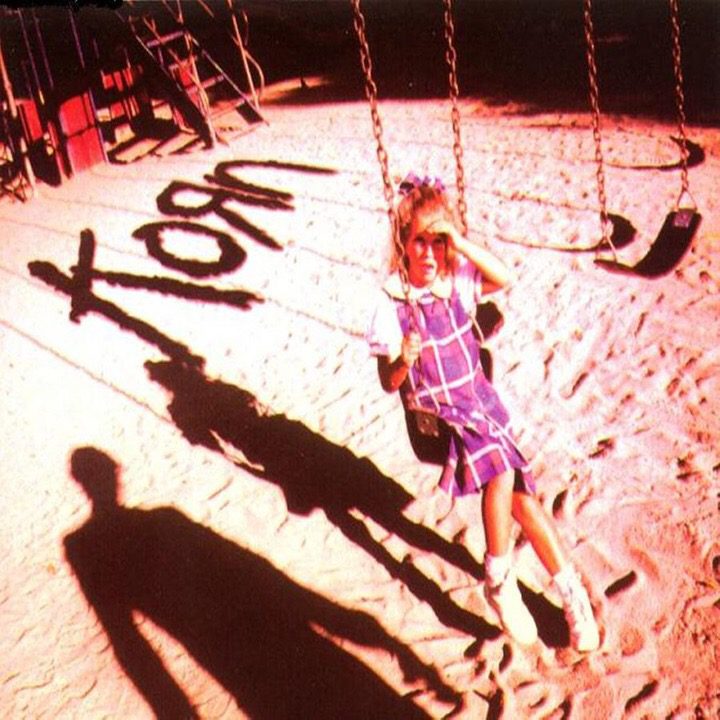 A girl in a purple dress sits on a swing, covering her eyes to look at a man, whose shadow is next to hers, both below the shadow of the name Korn.