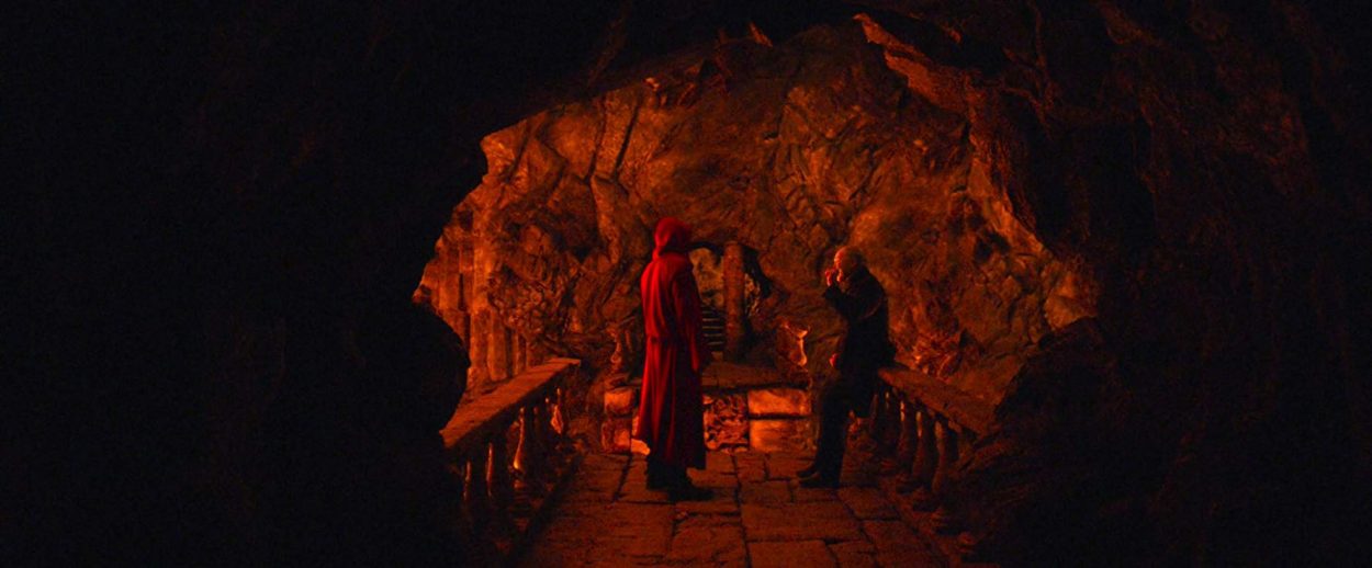 Jack and Virgil stand in a narrow cave mouth in front of a bridge