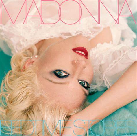 Madonna holds her arm under her head, as she lays on a pastel blue pillow. She is in a close up, upside down to our POV.