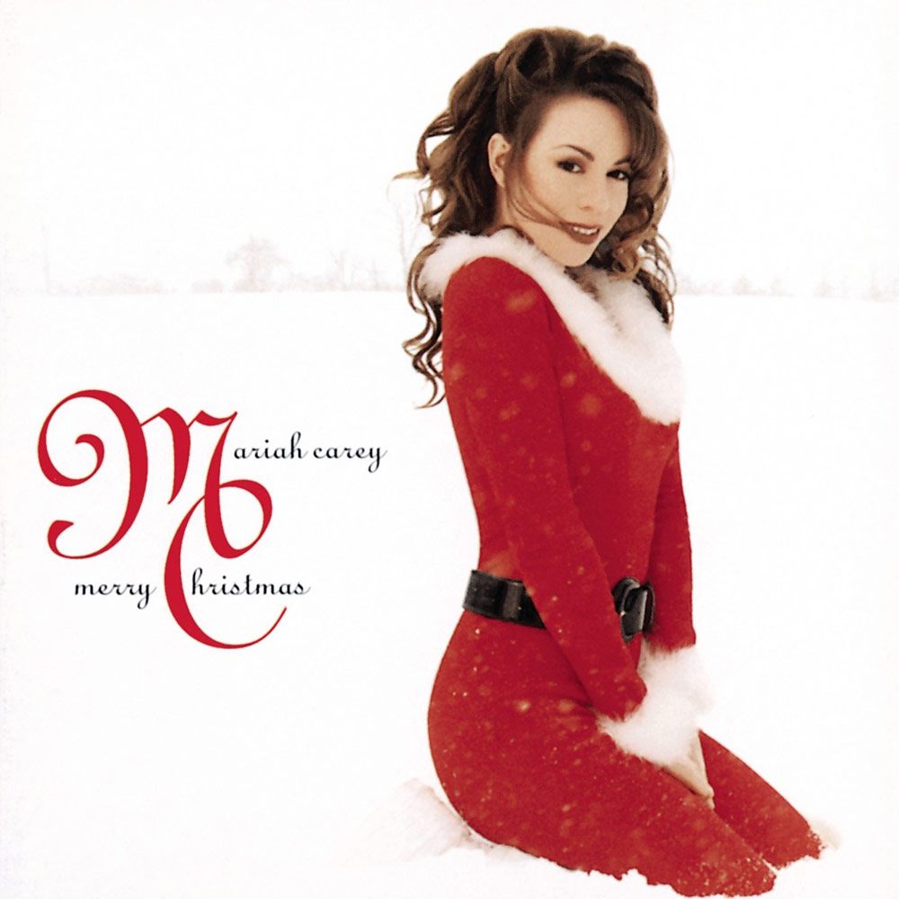 Mariah Carey is in a red Santa suit (no hat), coyly sitting outside in an otherwise white snowy scene.