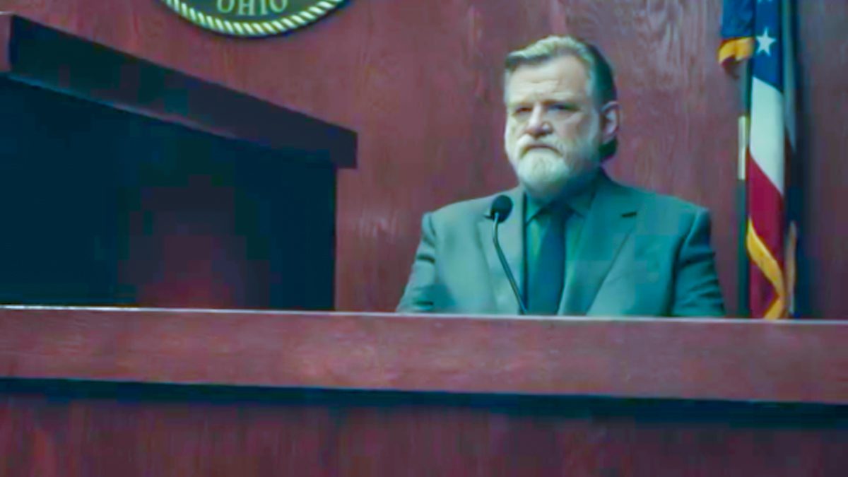 Bill Hodges sits on the witness stand, unhappy look on his face, with a US flag and Ohio seal in the background behind him.