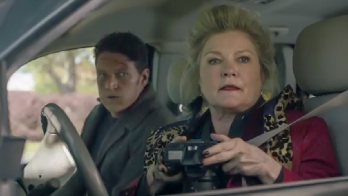 Alma and Morris sit in her car, white interior, Alma in the drivers seat with a camera pointed down, looking in the distance.