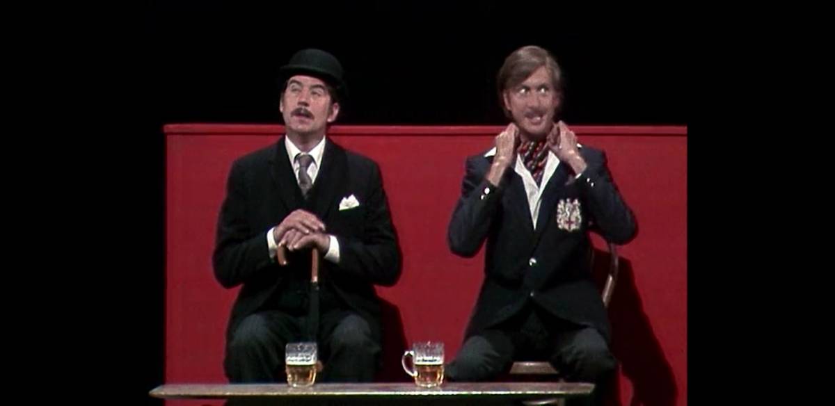 Terry Jones and Eric Idle performing on stage, dressed as a respectable man and a spin respectively