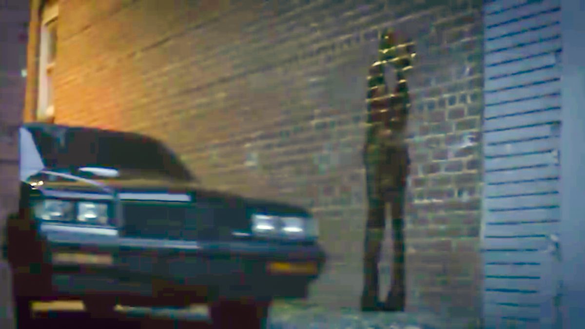Watchmen S1E2 - A car drives by a brick wall with a graffiti silhouette of a couple kissing.