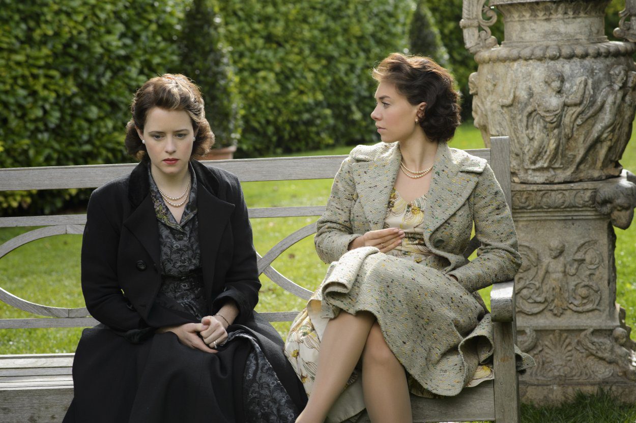 Elizabeth and Margaret sit talking on a bench on the palace grounds