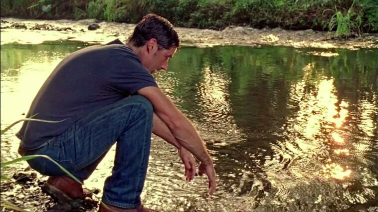 Jack looks at his hands as he kneels by the river