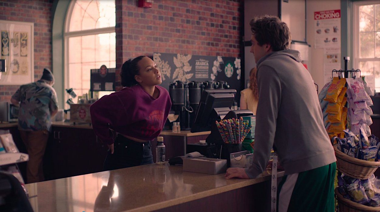 Chloe stands behind the counter at the coffee shop flirting with Brendan, who stands on the other side