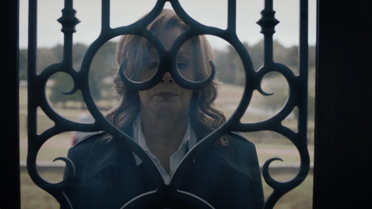 Watchmen - Laurie stands outside a glass door, the intricate iron work frames her face like a mask