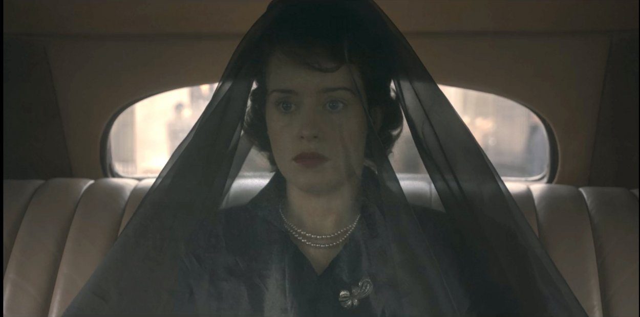 Elizabeth rides in the back of a car while wearing a long black veil 