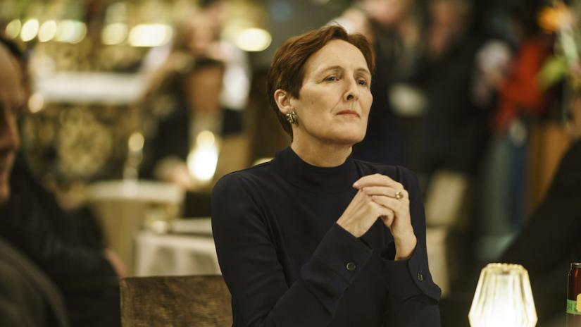 Fiona Shaw as her character in Killing Eve sitting at a table and clutching her hands