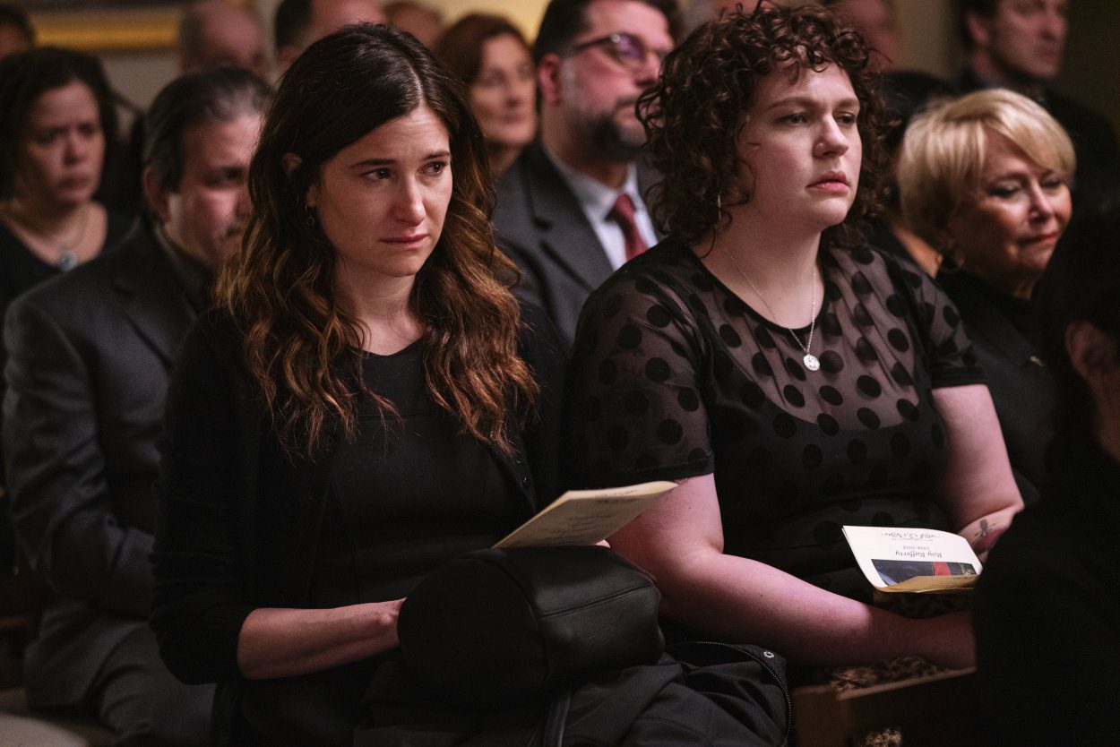 Eve and Amanda sit listening to the eulogy at Roy's funeral