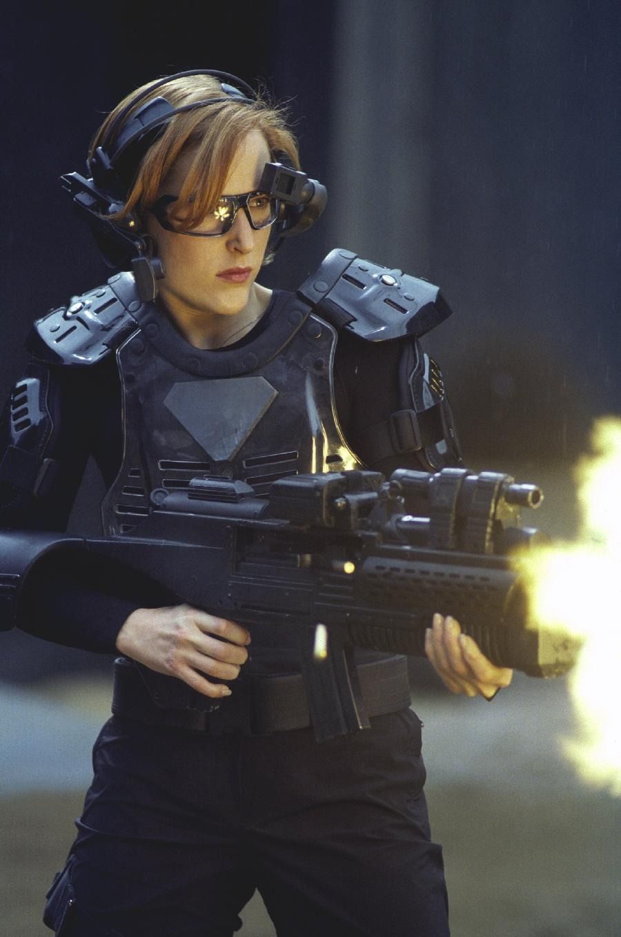 Scully fires a large automatic weapon while wearing a VR headset and other game gear.