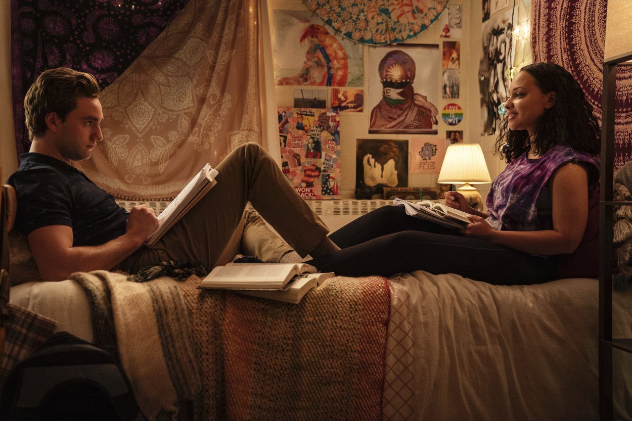 Brendan and Chloe sit on Chloe's bed looking at each other and surrounded by school books