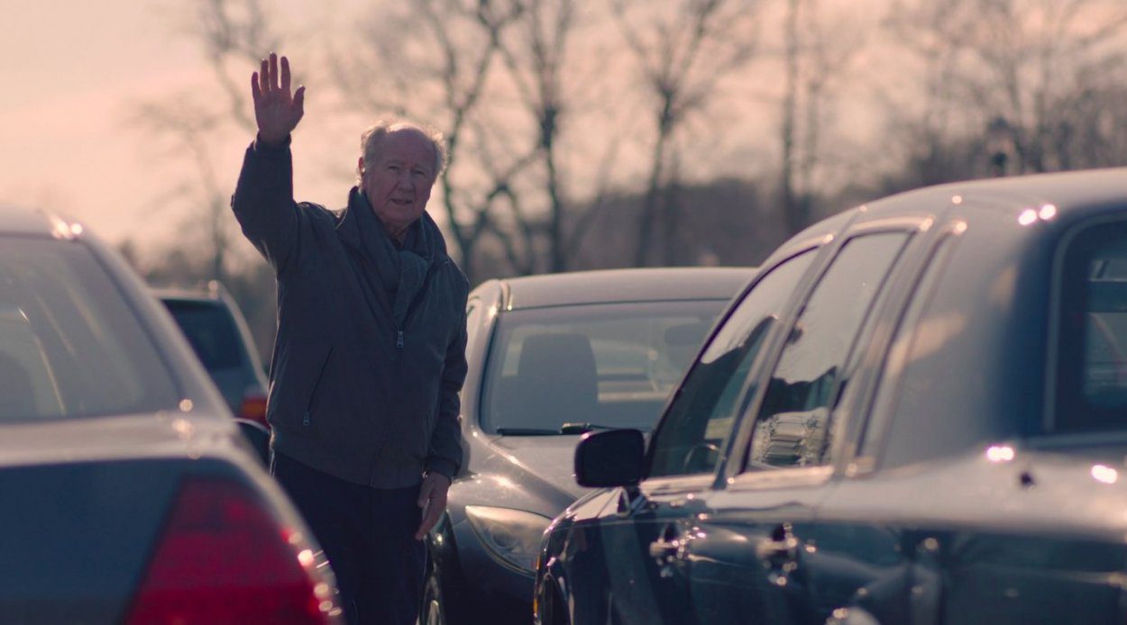 Roy Rafferty stands in a parking lot and waves to Eve