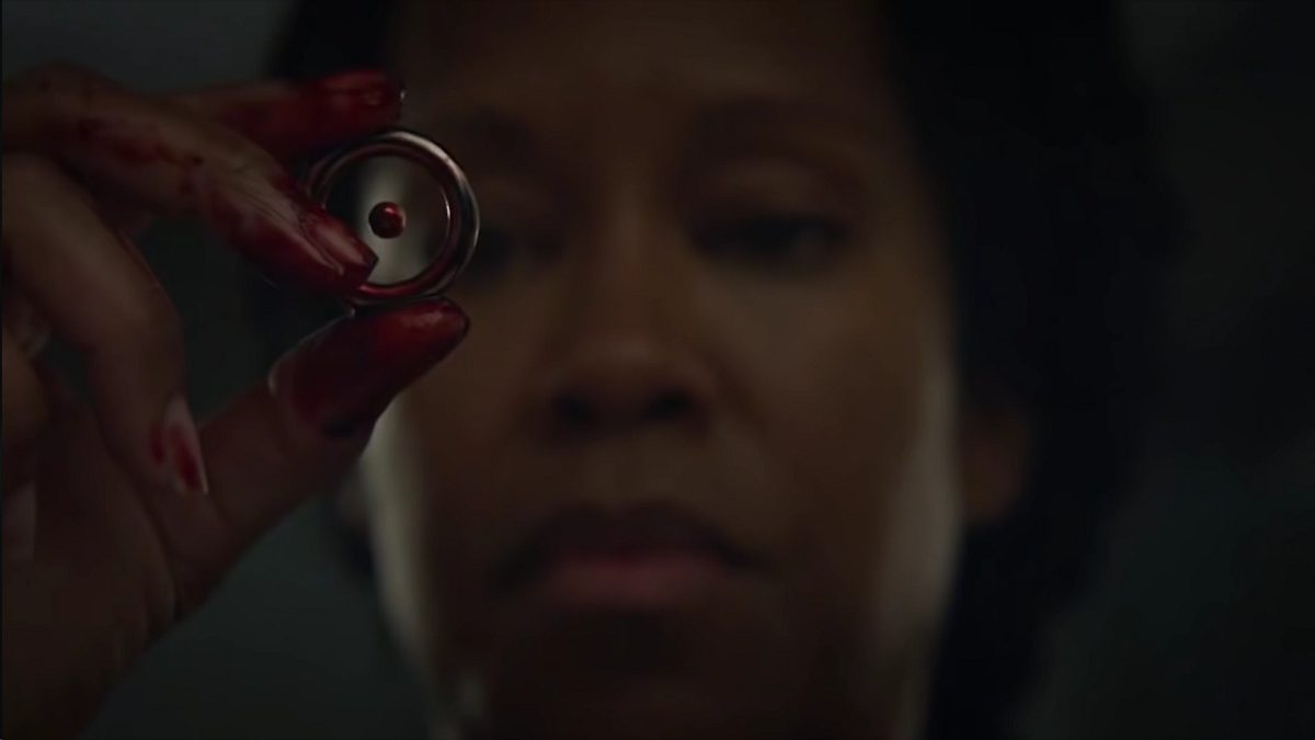 Watchmen - Angela holds a round chip to her eyes, held in bloody fingers