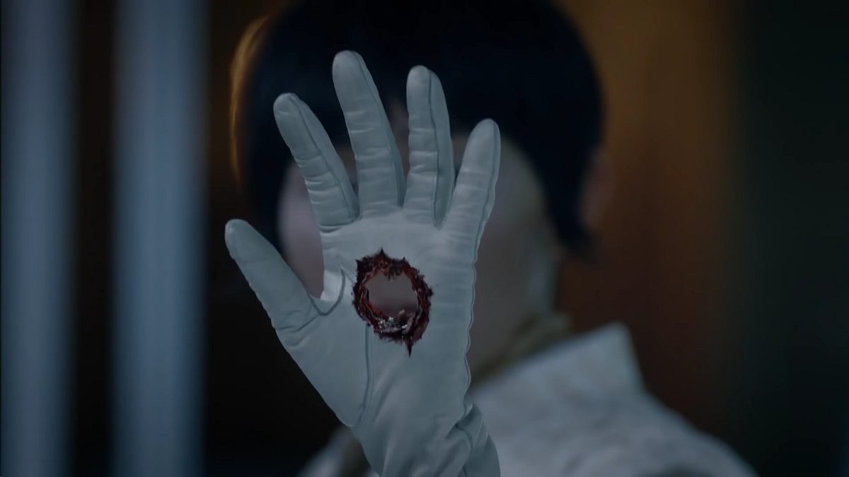 Watchmen - Lady Trieu holds her gloved hand in front of her face, with a hole punched clean through it