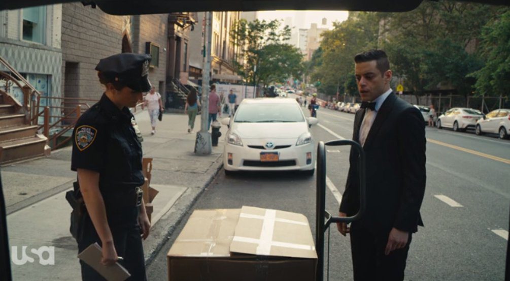 Dom as a cop confronts Elliot over a large box