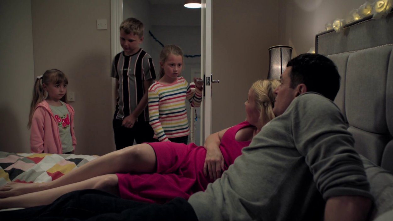 Gavin and Stacey kiss on the bed as their three children stand in the doorway interrupting them
