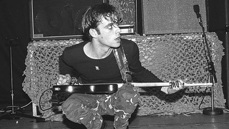 Richey Edwards on stage, squatting down with his guitar over his knees