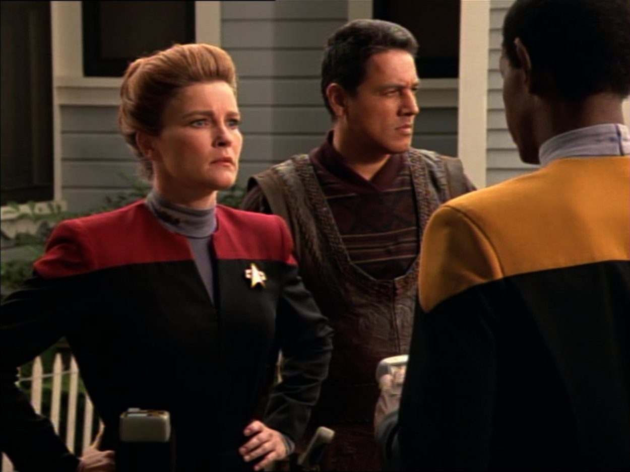 Janeway, Chakotay and Tuvok stand outside a house with a white picket fence