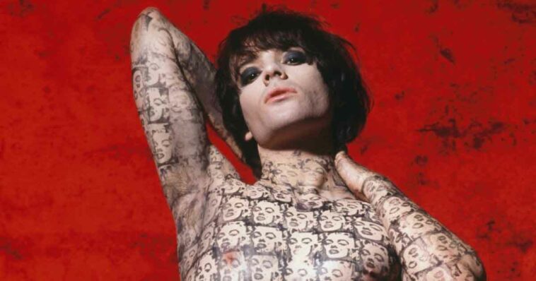 Richey Edwards poses against a red background, his body covered in Marilyn Monroe tattoos