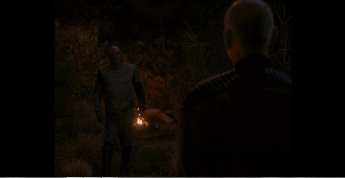 Dathon stands before a fire as he approaches Picard