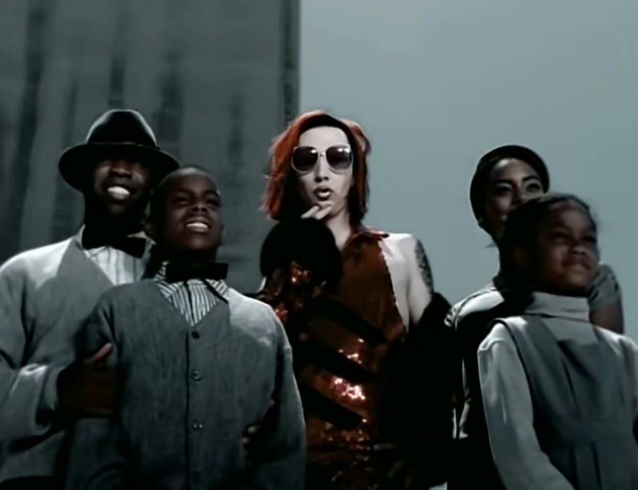 Marilyn Manson as an alien rock star posing for the camera, surrounded by people wearing grey clothes in "The Dope Show" music video