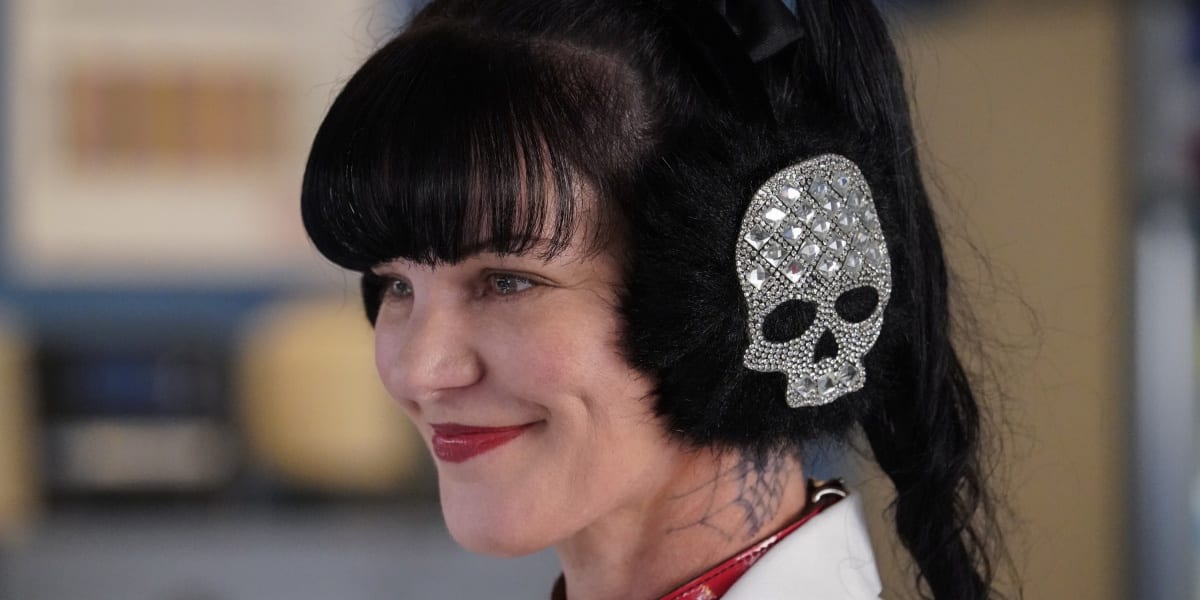 Abby smiling, looking ahead of her, wearing headphones with sparkly skulls on them in NCIS
