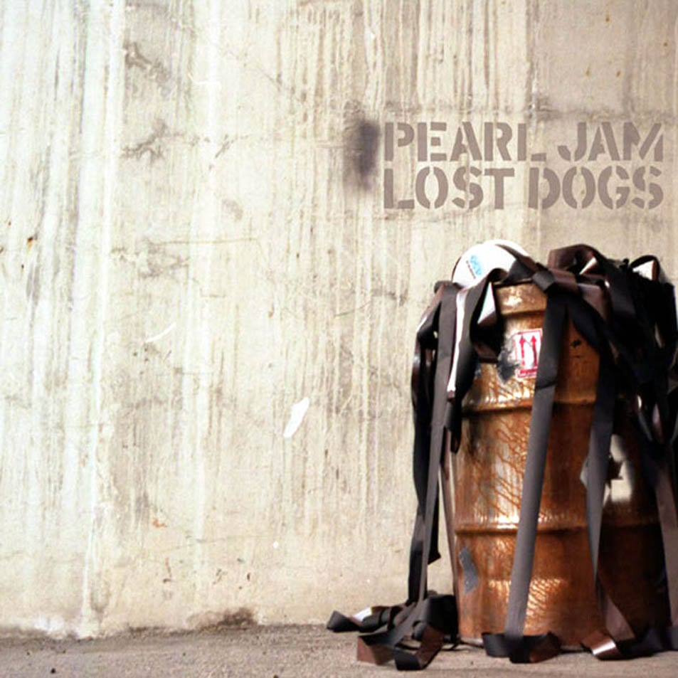 A gray concrete wall with “Pearl Jam Lost Dogs” appearing to be etched on it, with a brown barrel below it to the right.