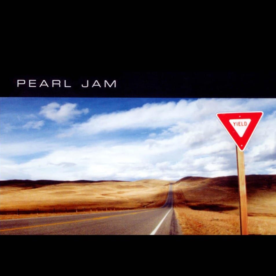 On a black background, an image of a blue sky, a brown landscape and a road with a yield sign on the side stretches across the bottom.