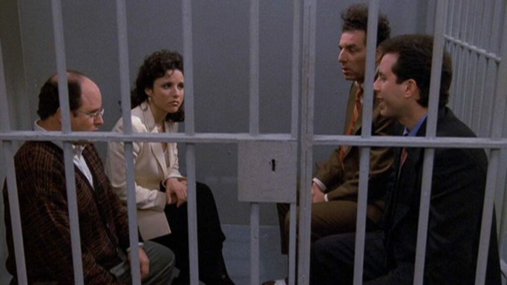 George, Elaine, Kramer, and Jerry sit behind bars in a jail cell