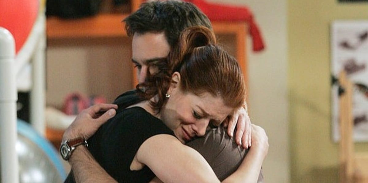 Will and Grace hugging, Grace looking sad, eyes closed, while Will comforts her